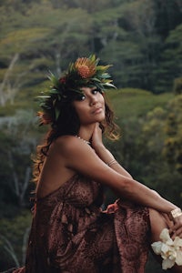 a woman wearing a hawaiian flower crown sitting on a rock