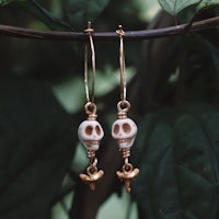 a pair of gold skull earrings hanging from a branch