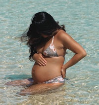 a pregnant woman in a bikini sitting in the water