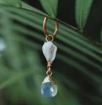 a blue stone and gold plated earring hanging from a palm tree