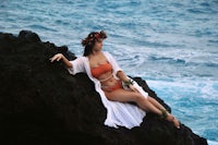 a woman in a bikini sitting on a rock by the ocean