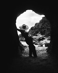 a black and white photo of a woman in a hat standing in a cave