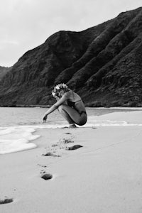 a woman kneeling on the beach with footprints in the sand