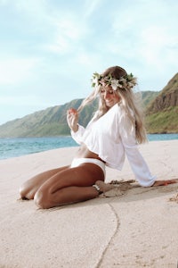 a blonde woman laying on the beach with a flower crown