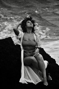 a woman sitting on a rock next to the ocean